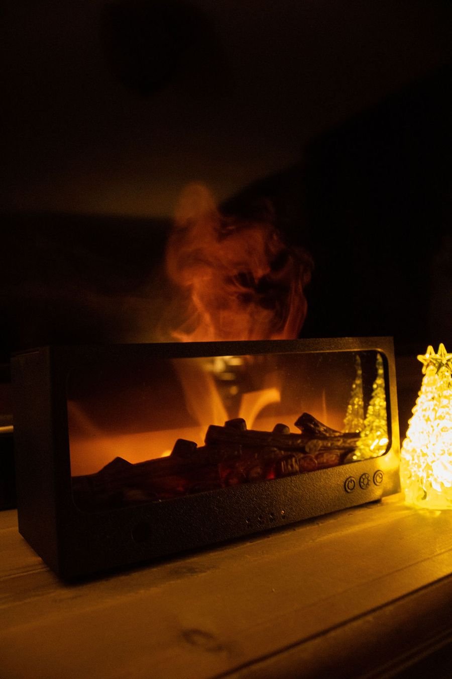 De zwarte Solafera Haard aan in een donkere kamer, met nevel erboven en een LED-boompje ernaast